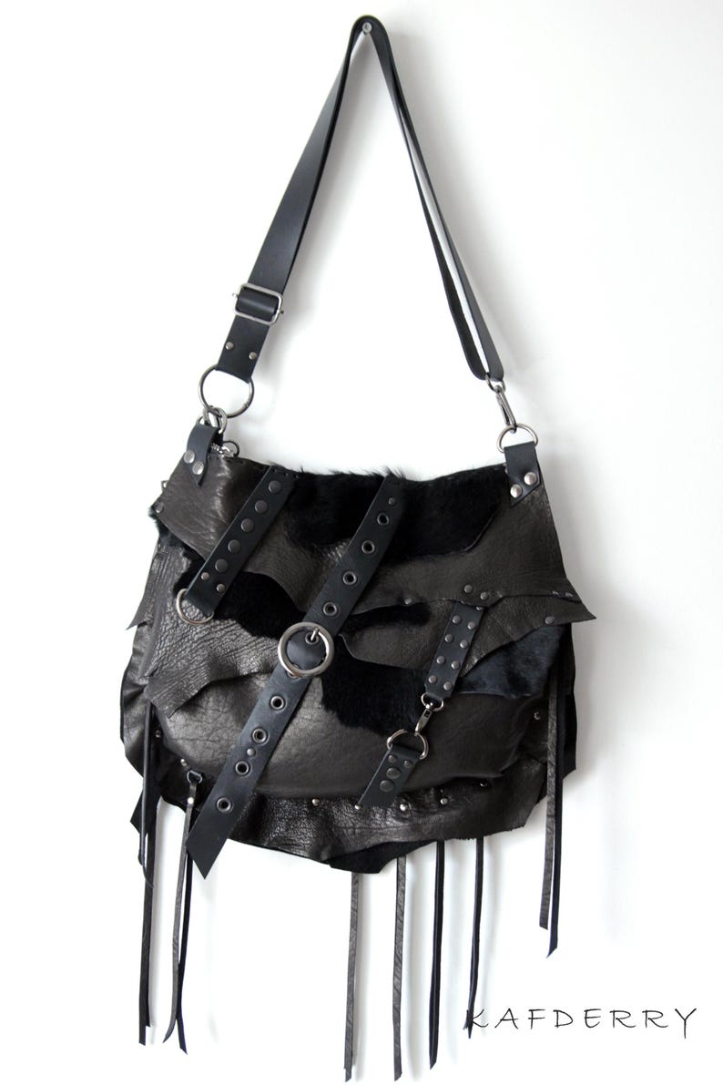 May include: Black leather shoulder bag with a unique, layered design. Features a long adjustable strap, metal hardware, and decorative fringe. The bag has a distinctive, edgy aesthetic.