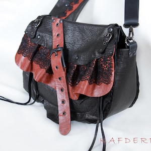 K&ouml;nnte beinhalten: Schwarze Leder-Umh&auml;ngetasche mit roten Leder- und schwarzen Spitzenakzenten. Die Tasche hat einen Klappenverschluss mit Schnalle und einen langen, verstellbaren Riemen. Einzigartiges, gotisches Design.