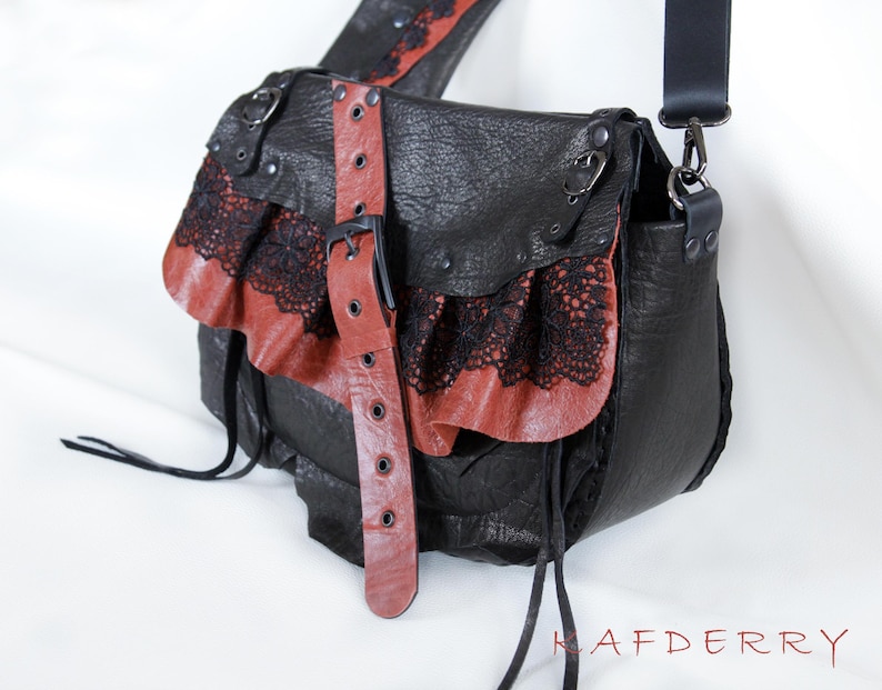 K&ouml;nnte beinhalten: Schwarze Leder-Umh&auml;ngetasche mit roten Leder- und schwarzen Spitzenakzenten. Die Tasche hat einen Klappenverschluss mit Schnalle und einen langen, verstellbaren Riemen. Einzigartiges, gotisches Design.