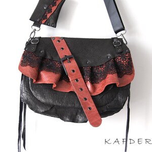 K&ouml;nnte beinhalten: Schwarze Leder-Umh&auml;ngetasche mit roter Lederklappe und schwarzem Spitzensaum. Die Tasche hat einen roten Lederriemen mit Schnalle und einen schwarzen Schulterriemen. Die Tasche ist mit Nieten verziert und tr&auml;gt das Wort "KAFDERRY".