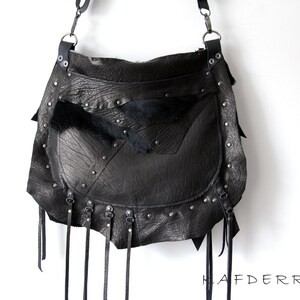 May include: Black leather shoulder bag with a flap closure, studded accents, and dangling leather straps. The bag features a textured leather exterior and a fur accent. The bag has a long adjustable strap and metal hardware.