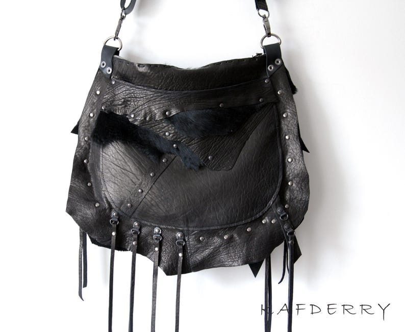May include: Black leather shoulder bag with a flap closure, studded accents, and dangling leather straps. The bag features a textured leather exterior and a fur accent. The bag has a long adjustable strap and metal hardware.