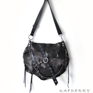 Puede incluir: Bolso de hombro de cuero negro con un dise&ntilde;o &uacute;nico. El bolso presenta una combinaci&oacute;n de texturas, incluyendo cuero, piel y cadenas met&aacute;licas. Tiene una correa larga y ajustable y correas decorativas de cuero con herrajes met&aacute;licos. El bolso est&aacute; suspendido sobre un fondo blanco.