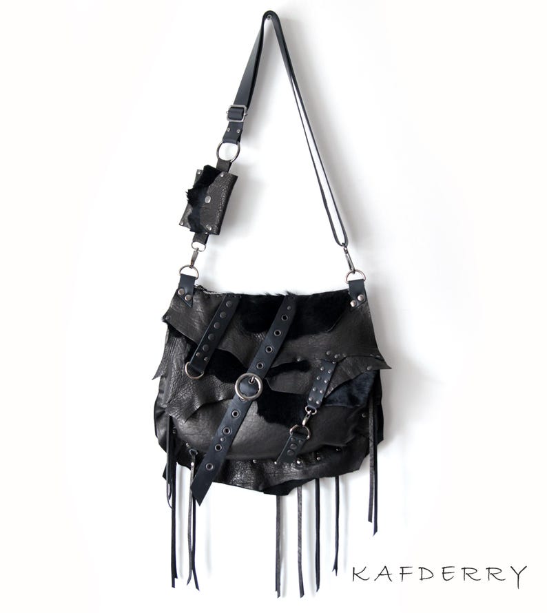 May include: Black leather shoulder bag with a layered design, featuring a small attached pouch. The bag has a long adjustable strap, metal hardware, and decorative fringe. The word "KAFDERRY" is printed at the bottom.