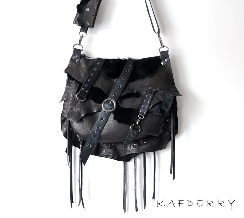 May include: Black leather shoulder bag with a unique, layered design. The bag features multiple straps, metal hardware, and fringe detailing. The bag has a flap closure and a long adjustable strap. The text "KAFDERRY" is visible at the bottom right.