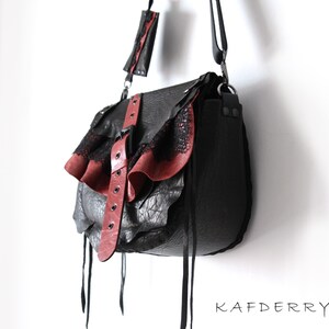 K&ouml;nnte beinhalten: Schwarze Leder-Umh&auml;ngetasche mit roten Akzenten. Die Tasche hat eine strukturierte Oberfl&auml;che, eine Klappe mit rotem Leder und Spitzentrimm, sowie einen roten Lederriemen mit Schnallen. Sie hat einen langen Schulterriemen und Lederkordeln.