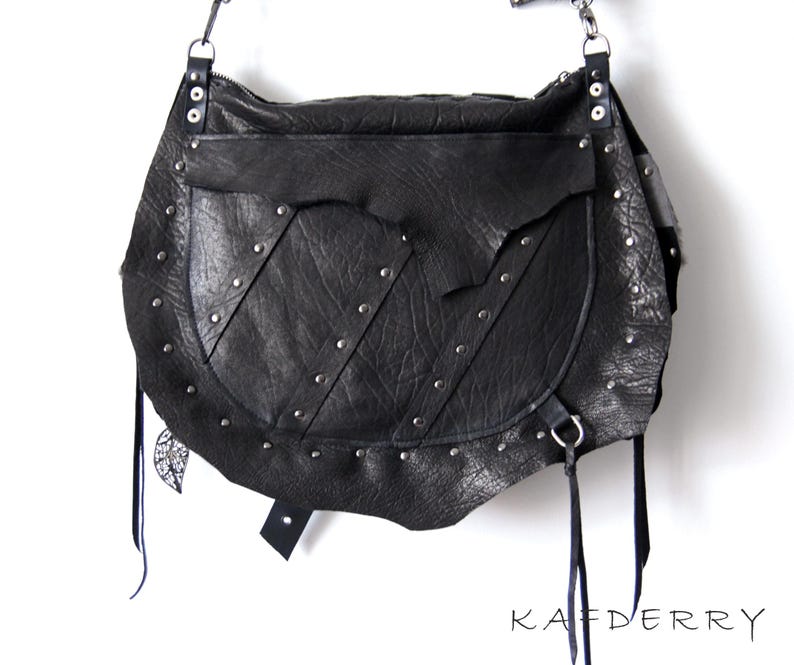 Puede incluir: Bolso de hombro de cuero negro con remaches plateados y un bolsillo con solapa. El bolso tiene un dise&ntilde;o texturizado &uacute;nico y largas borlas negras. La marca "KAFDERRY" est&aacute; impresa en la parte inferior.
