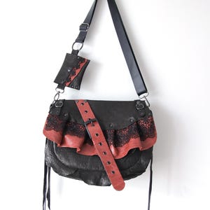 K&ouml;nnte beinhalten: Schwarze Leder-Umh&auml;ngetasche mit roter Leder- und schwarzer Spitzenr&uuml;sche. Die Tasche hat einen langen schwarzen Riemen und eine passende kleine Tasche. Ein roter Lederg&uuml;rtel mit Schnalle verl&auml;uft &uuml;ber die Vorderseite.