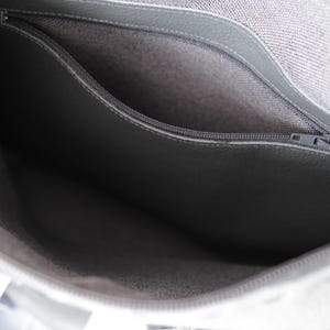 May include: Close-up of a grey handbag interior with a zipped pocket. The bag's interior is a lighter grey fabric, and the pocket is a darker grey material. The zip is silver.