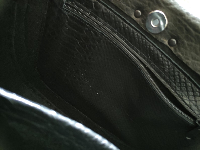 K&ouml;nnte beinhalten: Innenraum einer schwarzen Lederhandtasche mit Rei&szlig;verschlusstasche und Magnetverschluss. Der Innenraum ist mit einem strukturierten Stoff gef&uuml;ttert. Das Leder der Tasche hat ein leichtes Used-Aussehen.