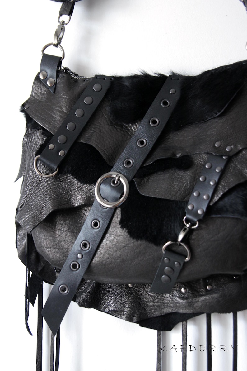 May include: Black leather shoulder bag with layered design and fur accents. Features multiple straps with metal hardware, including rivets and a large silver ring. The bag has a fringe detail.
