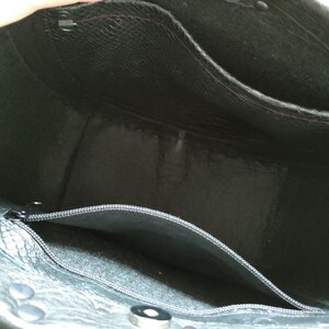 K&ouml;nnte beinhalten: Innenansicht einer schwarzen Leder-Tragetasche. Die Tasche hat mehrere Taschen, darunter eine mit Rei&szlig;verschluss, und ist mit einem kontrastierenden Material gef&uuml;ttert. Die Tasche hat Metallbeschl&auml;ge und eine strukturierte Au&szlig;enseite.