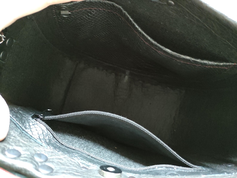 K&ouml;nnte beinhalten: Innenansicht einer schwarzen Leder-Tragetasche. Die Tasche hat mehrere Taschen, darunter eine mit Rei&szlig;verschluss, und ist mit einem kontrastierenden Material gef&uuml;ttert. Die Tasche hat Metallbeschl&auml;ge und eine strukturierte Au&szlig;enseite.