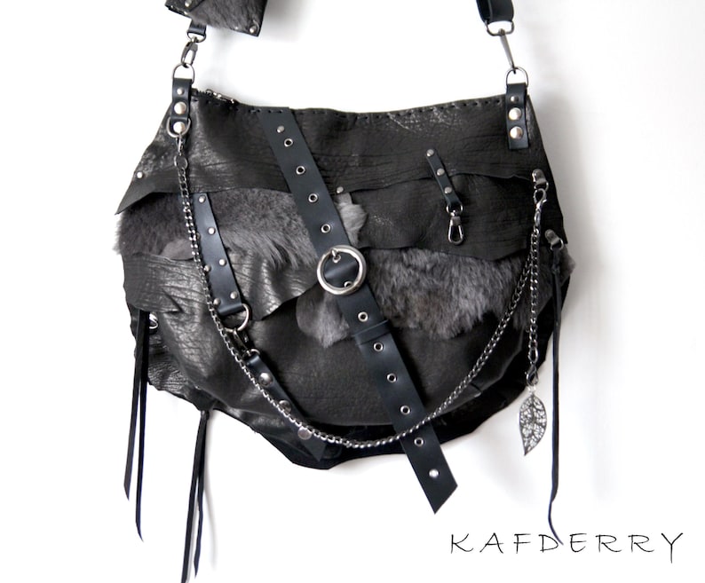 Puede incluir: Bolso de hombro de cuero negro con un dise&ntilde;o en capas y una cadena plateada. El bolso presenta una correa con un anillo de metal y un dije de hoja decorativa. La palabra "KAFDERRY" est&aacute; impresa en negro.