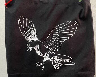May include: Black tote bag with a white graphic of a bird in flight. The bag has a shoulder strap and a rectangular shape. The bird design is detailed with white lines, and the bag appears to be made of canvas or a similar material.