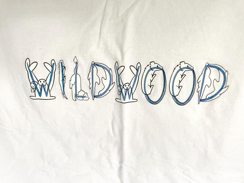 May include: White t-shirt with the word "WILDWOOD" in blue and white lettering. Each letter is designed with a unique illustration, including a seal, a cat, and other whimsical creatures.
