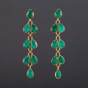 Pode incluir: Um par de brincos longos e pendentes com várias gotas de pedras preciosas verdes. Os brincos são feitos de metal dourado.