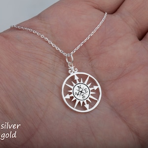 May include: A silver compass necklace with a circular pendant featuring a compass rose with the directions North, South, East, and West inscribed. The necklace has a delicate chain.