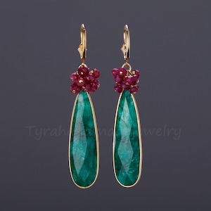 May include: Gold earrings featuring a teardrop-shaped emerald green gemstone and a cluster of ruby red stones.