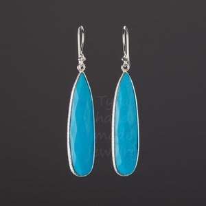 May include: A pair of silver dangle earrings with turquoise teardrop-shaped stones. The stones are faceted and have a light blue color.