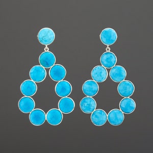 May include: A pair of turquoise and silver dangle earrings. Each earring features a teardrop-shaped design with a circle of turquoise stones.
