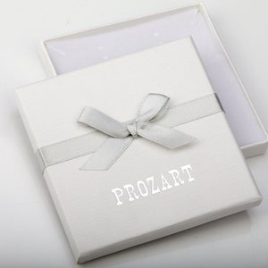 Op de afbeelding: Een witte geschenkdoos met een zilveren lint dat in een strik is geknoopt. De doos is open en onthult een wit interieur. Het woord "PROZART" is in zilver op de voorkant van de doos gedrukt.