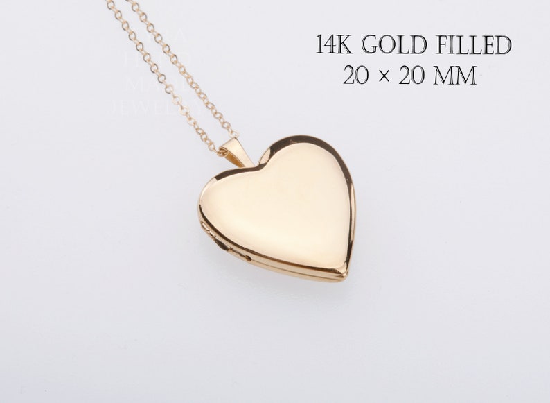 May include: A 14K gold filled heart-shaped locket pendant on a delicate gold chain. The text 14K GOLD FILLED 20 x 20 MM is printed in the upper right corner. The locket has a smooth, polished surface and a classic heart silhouette.