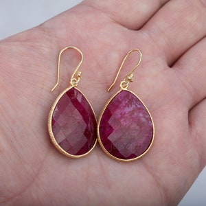 K&ouml;nnte beinhalten: Ein Paar goldene Ohrringe mit tropfenf&ouml;rmigen roten Edelstein-Anh&auml;ngern.