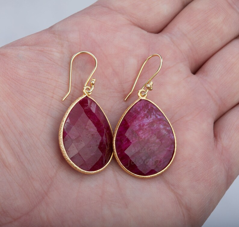 K&ouml;nnte beinhalten: Ein Paar goldene Ohrringe mit tropfenf&ouml;rmigen roten Edelstein-Anh&auml;ngern.