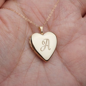 May include: A gold-toned heart-shaped locket pendant on a delicate chain. The front of the locket features an engraved script letter A. The text TYRA HAND MADE JEWELRY is visible in the upper right corner of the image, printed in a light font.