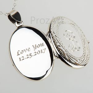 May include: Silver locket necklace with an engraved inscription that reads "Love You 12.25.2017". The locket is open to reveal a decorative design on the inside.