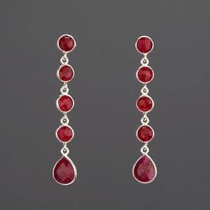 May include: A pair of silver dangle earrings with red gemstone drops. Each earring features five round red gemstones and a teardrop-shaped red gemstone.