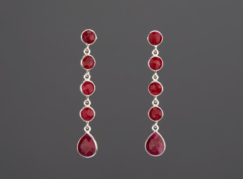 May include: A pair of silver dangle earrings with red gemstone drops. Each earring features five round red gemstones and a teardrop-shaped red gemstone.