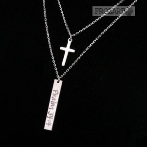 Puede incluir: Un collar plateado de dos capas con un colgante de cruz y un colgante rectangular con la inscripción "Salmo 23:4".