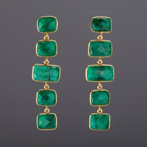 May include: A pair of long, gold earrings with five emerald green rectangular stones hanging from each earring.