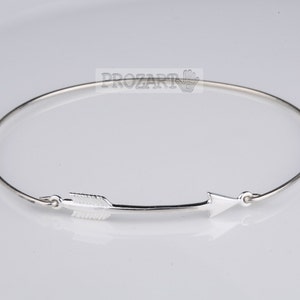 May include: A silver bangle bracelet with an arrow charm. The arrow is pointing to the right.