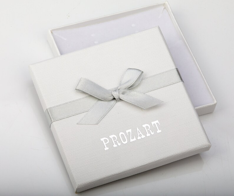May include: A white gift box with a silver ribbon and bow. The box has the word "PROZART" printed on the front in silver lettering.