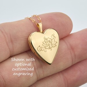 May include: A gold-toned heart-shaped locket pendant suspended from a delicate matching chain. The front surface of the locket features a fine-line engraved lotus flower design with swirling accents and the text Shown with optional customized engraving.