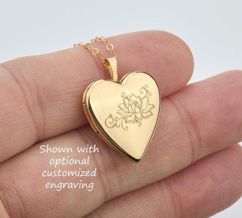 May include: A gold-toned heart-shaped locket pendant suspended from a delicate matching chain. The front surface of the locket features a fine-line engraved lotus flower design with swirling accents and the text Shown with optional customized engraving.