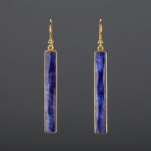 Może przedstawiać: Para złotych kolczyków z długimi, prostokątnymi, niebieskimi kamieniami szlachetnymi.