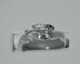 Puede incluir: Anillo plateado con un diseño detallado de conejo. El anillo presenta un acabado texturizado, con la figura del conejo en la parte superior. El fondo blanco resalta los intrincados detalles del anillo, ideal como joya.