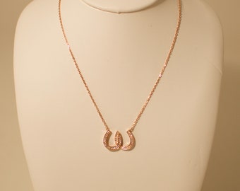 May include: A gold necklace with two interlocking horseshoe pendants adorned with small clear stones.