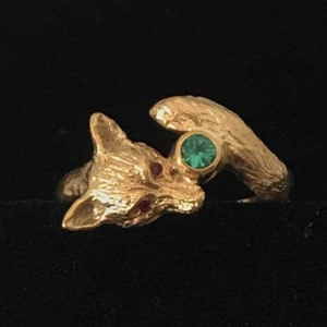 Puede incluir: Un anillo de oro con un diseño de zorro detallado con una piedra preciosa verde engastada en el centro. Los ojos del zorro están acentuados con piedras preciosas rojas.