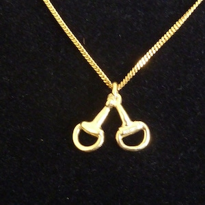 May include: A gold chain necklace with a gold pendant in the shape of two horse bits.