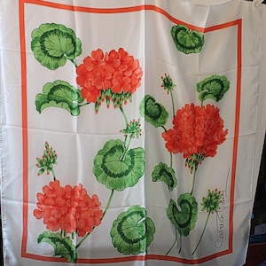 Puede incluir: Pañuelo cuadrado blanco con un diseño floral. Presenta flores de geranio naranja con hojas y tallos verdes. Un borde naranja enmarca el diseño. El pañuelo está firmado "Carol G. Vasey".