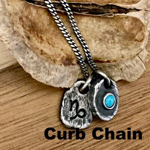 May include: A silver curb chain necklace with two pendants. One pendant features the Capricorn symbol, and the other has a small turquoise stone. The text "Curb Chain" is at the bottom of the image.