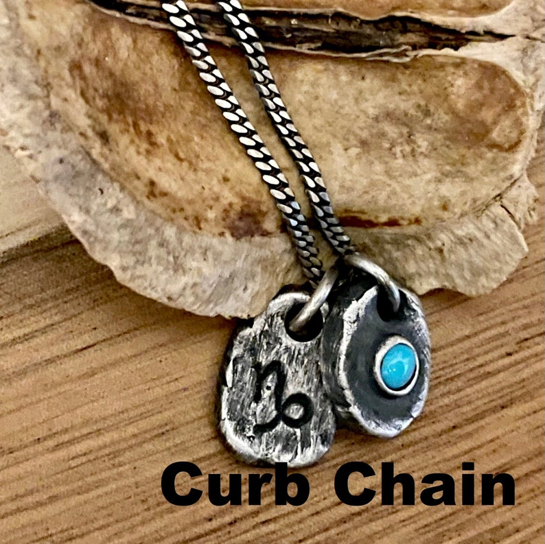 May include: A silver curb chain necklace with two pendants. One pendant features the Capricorn symbol, and the other has a small turquoise stone. The text "Curb Chain" is at the bottom of the image.