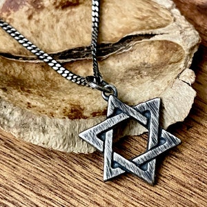 May include: A silver chain necklace with a silver Star of David pendant. The pendant is textured and has a brushed finish.