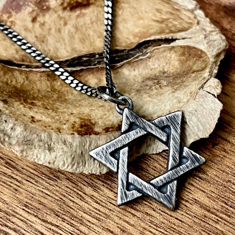 May include: A silver chain necklace with a silver Star of David pendant. The pendant is textured and has a brushed finish.