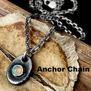 May include: A silver-toned necklace with a small, oval pendant. The pendant features a colorful opal stone set in a textured metal frame. The chain is a linked design. The words "Anchor Chain" are printed on the image.